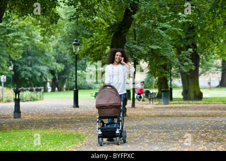 Junger Mann schieben Kinderwagen im Park und telefonieren mit Handy Stockfoto