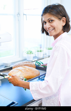 Porträt der Frau hält Brot auf Tablett in Küche Stockfoto