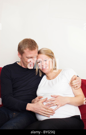 Mann mit schwangeren Frau sitzend auf Sofa hält die Hand auf den Bauch Stockfoto