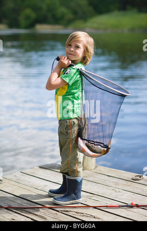 Junge hält net mit fangen Fische, stehend auf Steg Stockfoto