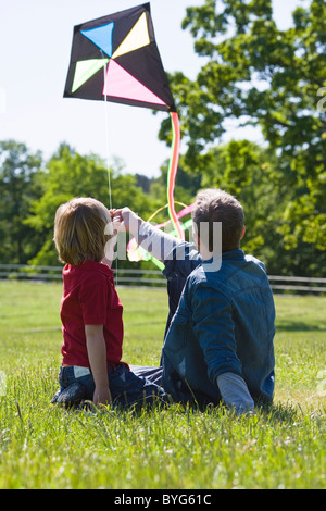 Vater und Sohn sitzen auf Rasen mit kite Stockfoto