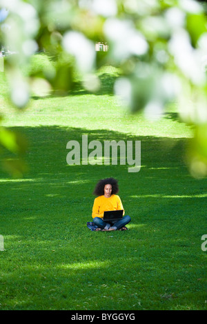 Junger Mann mit Afro-Haar sitzen auf Rasen mit laptop Stockfoto