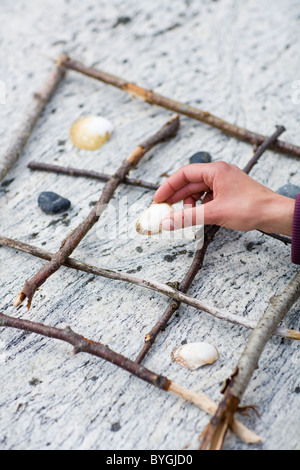 Menschliche Hand halten Kiesel über Tic Tac Toe am Strand Stockfoto