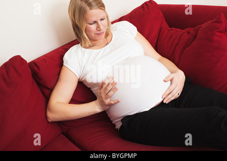 Schwangere Frau berühren Magen auf sofa Stockfoto