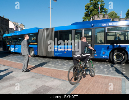 Fußgänger und Radfahrer im Stadtzentrum von Cardiff warten auf eine kurvenreiche Bus Baycar, überqueren Sie die Straße Cardiff Wales UK Stockfoto