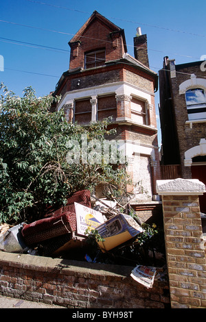 Müll im Vordergrund der Garten mit Brettern vernagelt Haus. South London Vereinigtes Königreich. Stockfoto