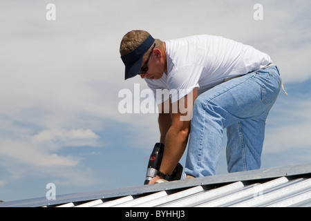 Bauarbeiter eine Bohrmaschine verwendet, um eine Mütze zu befestigen die oben auf ein Blech Bedachung Job mit Schrauben. Stockfoto