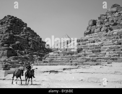 Ein Junge reitet auf einem Pferd und führt ein anderes vor Pyramiden in Gizeh, Ägypten. Stockfoto