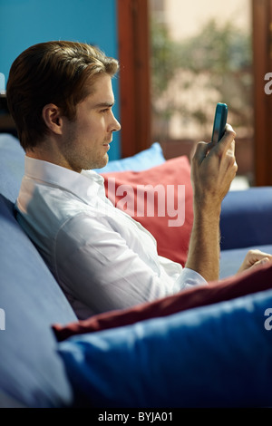 Mann auf Sofa zu Hause sitzen und Schreiben von SMS auf dem Handy. Vertikale Form, Seitenansicht, Hüfte aufwärts Stockfoto