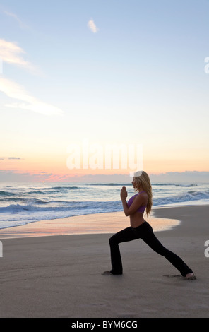 Schöne junge Frau praktizieren Yoga am Strand bei Sonnenaufgang oder Sonnenuntergang Stockfoto