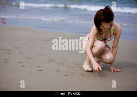 Junge Frau Zeichnung auf Sand Stockfoto