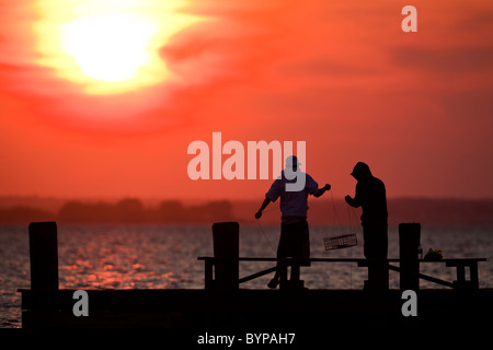 USA, New Jersey, Lavallette, Silhouette der jungen Männer Angeln für Krabben vom Pier bei Sonnenuntergang am Sommerabend Stockfoto