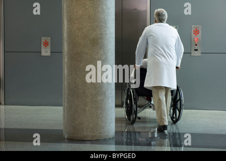 Arzt Patient im Rollstuhl in Richtung Aufzug schieben Stockfoto