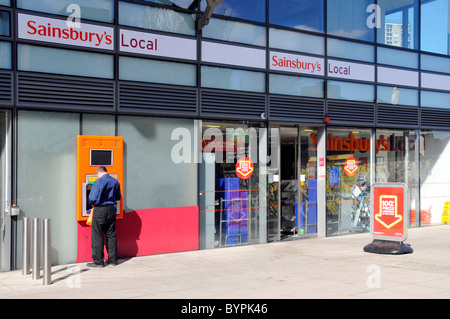 Sainsburys lokalen Supermarkt store Eingang und Rückansicht der Mann mit externen ATM Loch in der Wand, in der Kasse Maschine London England Großbritannien Stockfoto