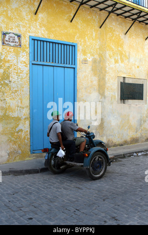 Motorrad und Seite Auto vor einer gelben Wand und blaue Tür in Calle de Los Mercaderes Straße, Havanna, Kuba. Stockfoto