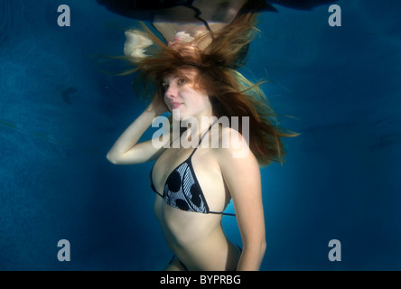 Eine junge Frau mit großen Haar posiert in einem Pool unter Wasser Stockfoto