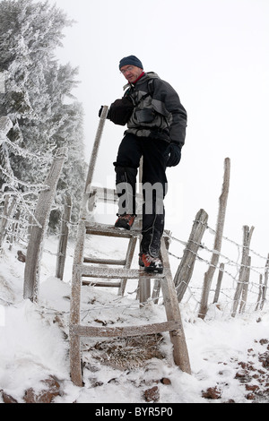 Im Winter ist ein Wanderer Klettern einen Stil in der Auvergne Vulkane Nature Reserve (Frankreich). Randonneur Franchissant un Échalier. Stockfoto