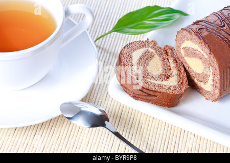 Closeup Swiss roll mit Kondensmilch Creme auf einem weißen Teller und eine Tasse Tee Stockfoto