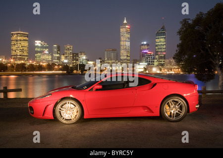 Ferrari F430 Sportwagen sitzt neben dem Swan River mit Perth Skyline im Hintergrund, Western Australia. Stockfoto