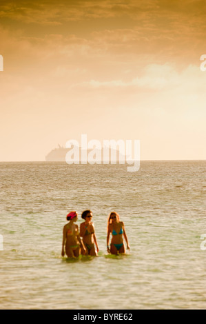 Nicht identifizierte Kreuzfahrtschiff vor der Küste der Insel Roatan, Honduras. Drei Frauen laufen im Meer im Vordergrund. Stockfoto