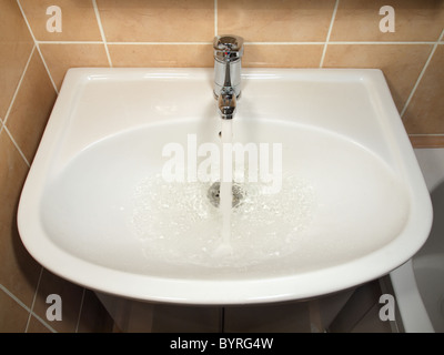 Weiße moderne Keramik Waschbecken und Chrom Wasserhahn, Wasser läuft. Stockfoto