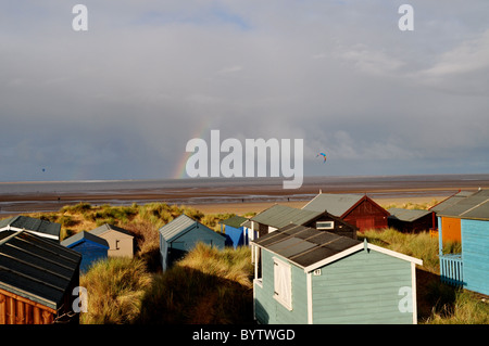 Strandhütten auf der englischen Küste, Regenbogen und Kite-Surfer im Winter Komplementärfarben. Stockfoto