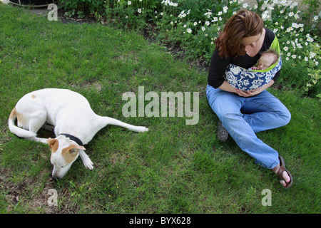 Eine Frau sitzt auf einer grünen Wiese mit einem Baby neben einem Hund. Stockfoto