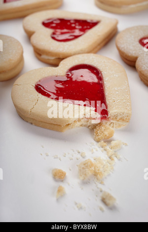 Foto von herzförmige Kekse gefüllt mit roter Marmelade auf einem weißen Hintergrund. Enthält gebrochen Keks und Krümel. Valentinstag-Konzept. Stockfoto