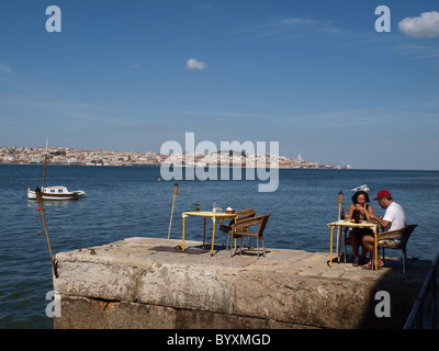 Touristen, die mit einer Mahlzeit vom Fluss Tejo mit Lissabon im Hintergrund Stockfoto