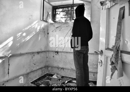 Männliche Kapuzengestalt Blick durch Fenster des verlassenen Hauses. Schwarz und weiß. Stockfoto