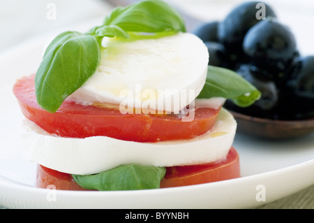 Tomaten-Mozzarella-Stapel mit Oliven als Closeup auf einem weißen Teller Stockfoto