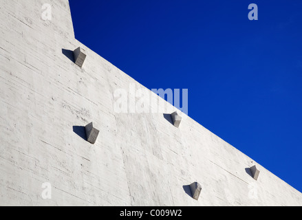 Teil einer Sonne beleuchtet konkrete Lager Wand mit scharfen Winkeln, ragt Aufbauten, und gegen einen dunkelblauen Himmel Stockfoto