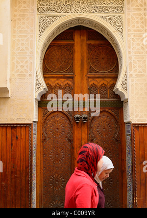 Zwei Frauen in roten Hijab verzierten Holztüren einer Moschee in Fes el Bali Medina Fes Marokko Nordafrika vorbei Stockfoto