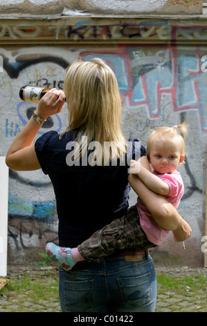 Junge Frau hält eine Zigarette und trinken aus einer Bierflasche, kleines Mädchen, 2 Jahre Stockfoto