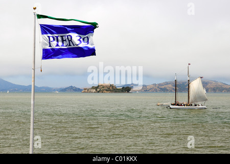 Flagge von Pier 39 und ein historisches Segelschiff in der Bucht von San Francisco, Alcatraz Island auf der Rückseite, San Francisco, Kalifornien, USA Stockfoto