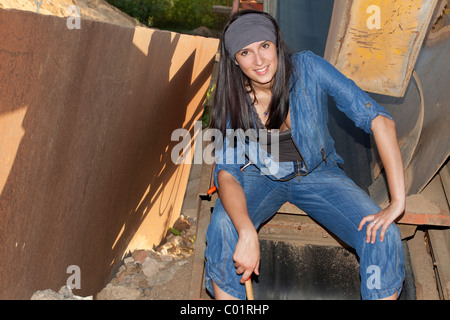 Junge Frau trägt Denim-Overalls vor Industriemaschinen Stockfoto