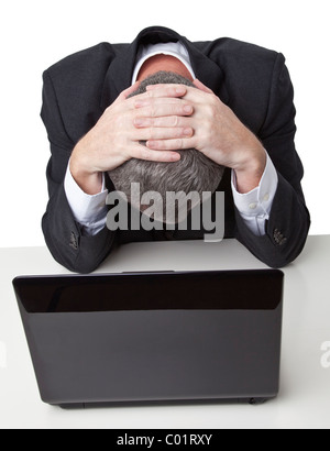 Geschäftsmann hielt seinen Kopf in seine Hände vor einem schwarzen Laptop, vor einem weißen Hintergrund isoliert Stockfoto