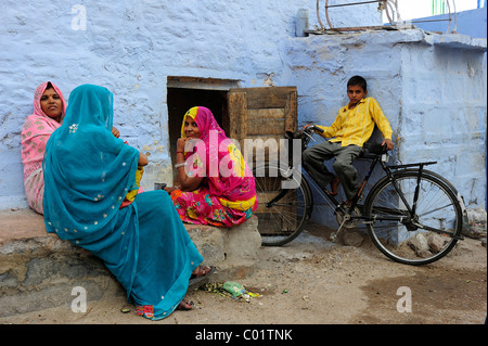 Drei indische Frauen tragen bunte Saris sprechen vor ihrem Haus ein Junge sitzt auf seinem Fahrrad Stockfoto