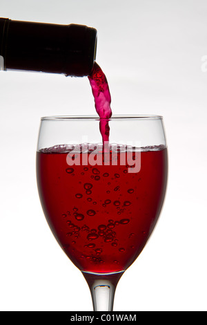 Rotwein in Strömen aus eine Flasche Wein in ein Glas Wein auf weißem Hintergrund Stockfoto