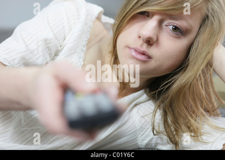 Junge Frau mit Fernbedienung in der Hand liegend Stockfoto