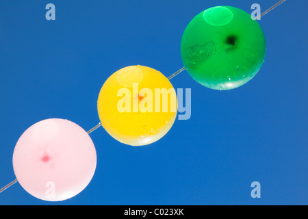 Farbige Luftballons mit Wassertropfen hängen auf einer Wäscheleine mit blauem Himmel als Hintergrund, von unten Stockfoto