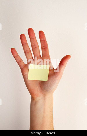 die Hand einer Frau mit einem leeren gelben Zettel geklebt auf die Handfläche und aus weißem Hintergrund Stockfoto