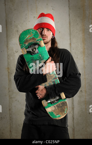 Junger Mann hält Skateboard über konkrete Grunge Hintergrund Stockfoto