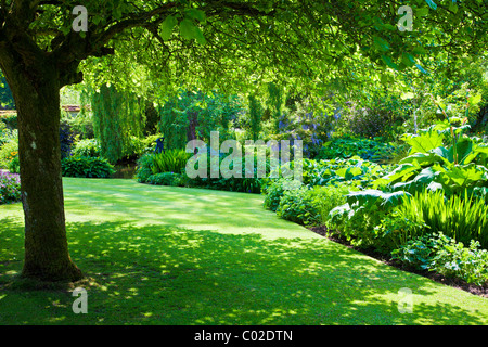 Eine schattige Ecke unter einem Baum am Ufer von einem Zierteich Garten in einem englischen Landhaus-Garten Stockfoto