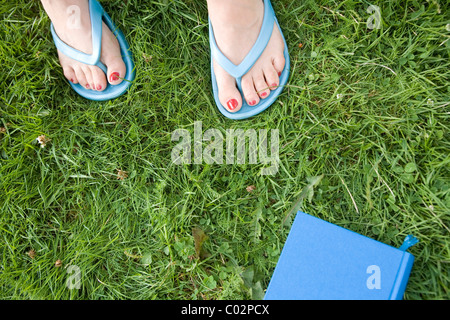 Füße in Flip Flops und buchen Sie auf einer Wiese Stockfoto