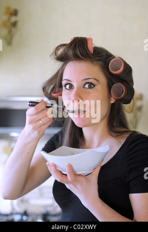 Junge Frau trägt Rollen in Haar mit Frühstück hetzen zur Arbeit am Morgen zu kommen Stockfoto