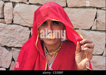 Porträt einer jungen indischen Frau trägt einen roten Sari und eine goldene Nasenring vor einer Steinmauer, Bishnoi ethnische Gruppe Stockfoto