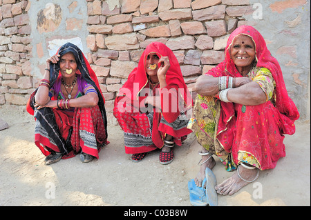 Drei indische Frauen mit goldener Nase-Ringen in traditioneller Kleidung vor einer Steinmauer auf dem Boden sitzen Stockfoto