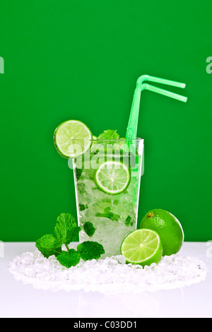 Foto von einem Mojito cocktail mit frischer Limette und Minze Blätter auf einen weißen Balken mit grünem Hintergrund. Stockfoto