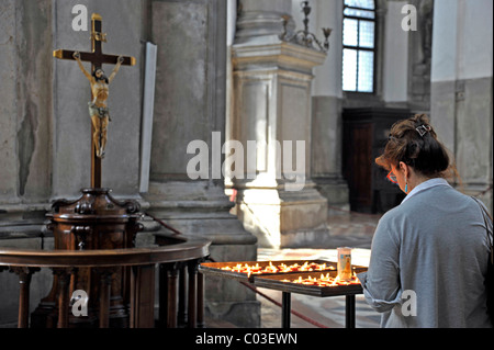 Frau im Gebet mit Kerzen vor Jesus am Kreuz im Hauptschiff der Kirche Santa Maria della Salute, Venedig Stockfoto